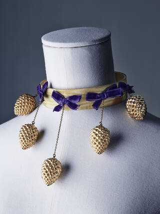 gold necklace with purple bows and hanging gold pinecones on light grey mannequin neck