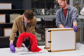 Two people unpack a hat from storage in a study centre