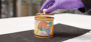 a gloved hand opens a ceramic jar